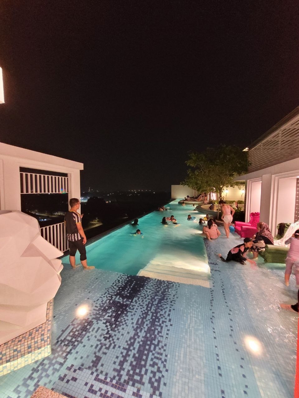 Rooftop infinity sky pool lit up at night with guests swimming