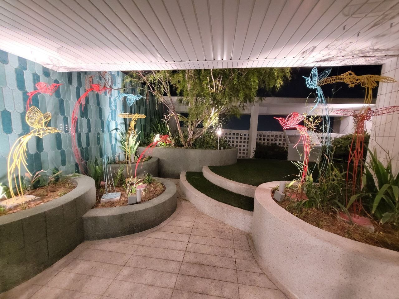 Sheltered garden nook with colourful wire bird sculptures and planters